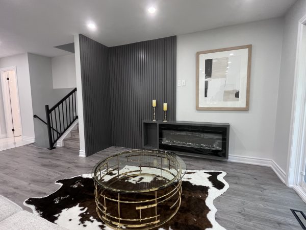 “Modern living room renovation with dark accent wall, built-in electric fireplace, and gold round coffee table — interior makeover by Delghavi Design & Build in Vaughan.”