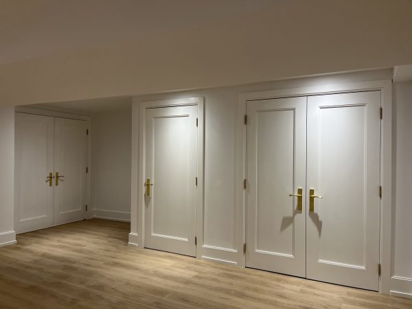 “Custom white MDF interior doors with gold hardware and detailed trim work in a renovated basement hallway — premium millwork installation by Delghavi Design & Build in Aurora.”