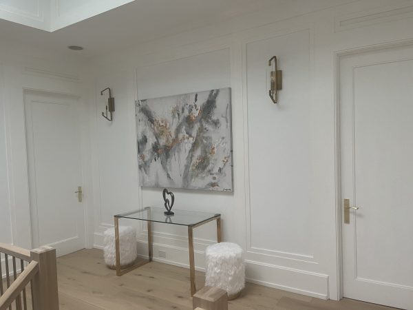 Elegant hallway with custom white MDF wall paneling, gold hardware, modern sconces, and glass console table — premium interior millwork by Delghavi Design & Build in Aroura