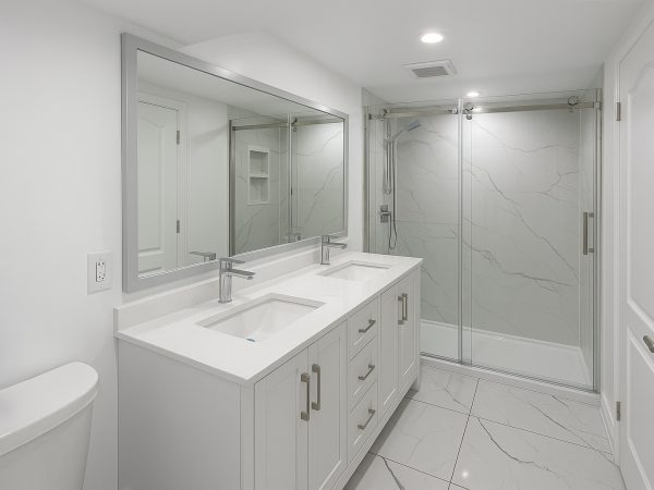 Bright modern bathroom renovation with double vanity, large frameless shower, and marble tile flooring by Delghavi Design in Ontario