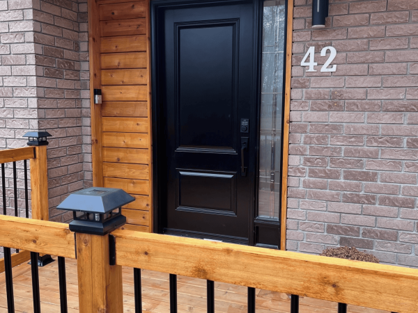 Custom front entrance renovation in Toronto with black door, cedar wood accents, and brick exterior by Delghavi Design and Build