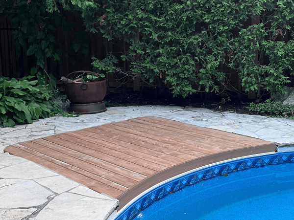 Curved wood pool deck integrated with stone patio by Delghavi Design & Build in Aurora