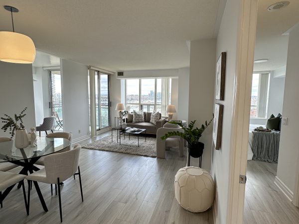 Open-concept condo living and dining area with floor-to-ceiling windows, modern furniture, and light wood flooring by Delghavi Design and Build