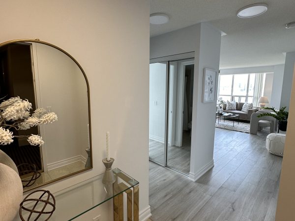 Bright condo entryway with glass console table, arched mirror, and view into modern open-concept living room