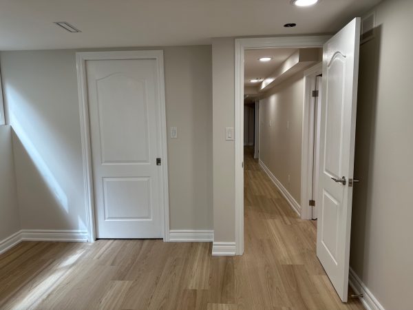 Finished basement hallway with light wood flooring, white interior doors, crown molding, and recessed LED lighting.