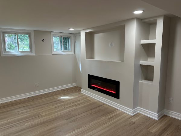 Finished basement feature wall with built-in electric fireplace, recessed shelving, and pot lighting.
