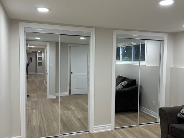 Finished basement bedroom with mirrored sliding closet doors, light wood flooring, and recessed lighting.